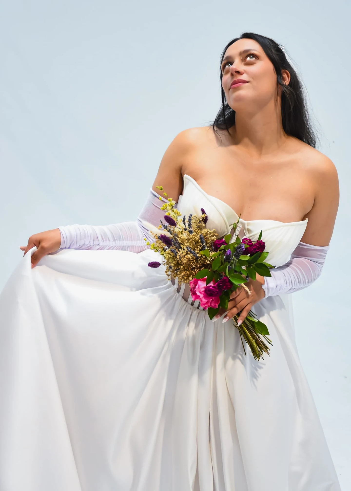 Novia con vestido de corsé a medida, guantes largos y ramo de flores silvestres