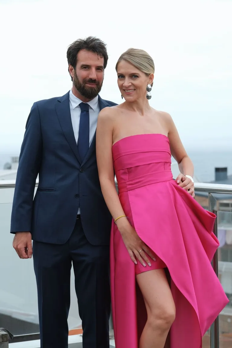 Novio con traje azul marino a medida de cuerpo entero en una terraza de A Coruña, junto a una invitada con vestido fucsia
